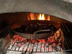 Châtaignes grillées au four à bois, dans une poêle posée sur une grille au-dessus des braises